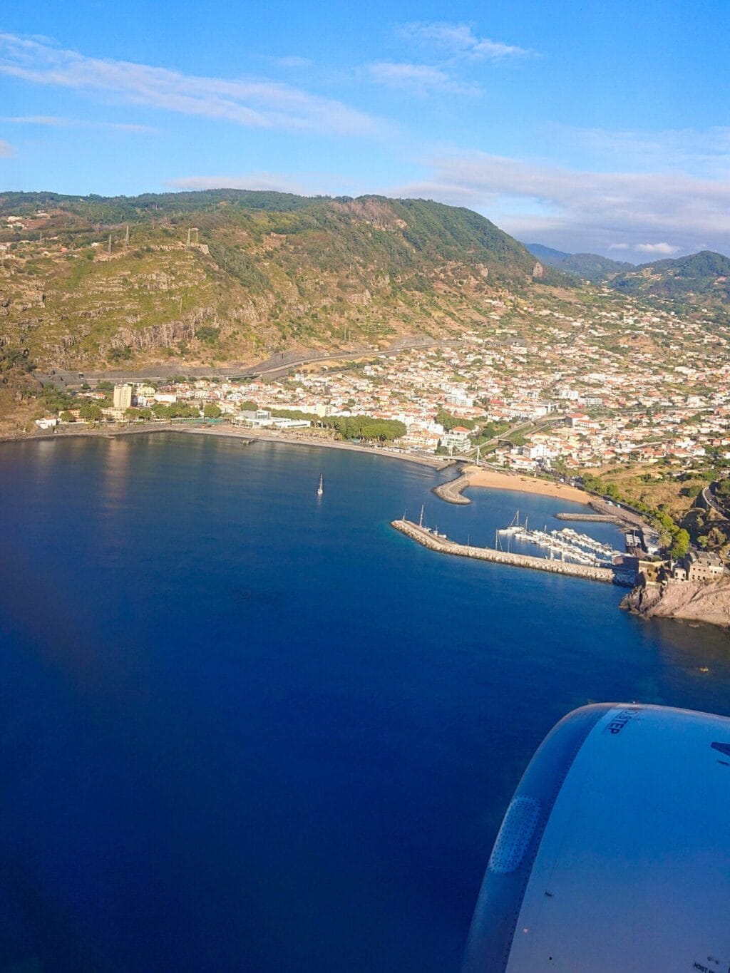 Luftbild beim Landeanflug auf die Insel Madeira mit Blick auf eine Meeresbucht, Hafen, Kleinstadt und Berge im Hintergrund